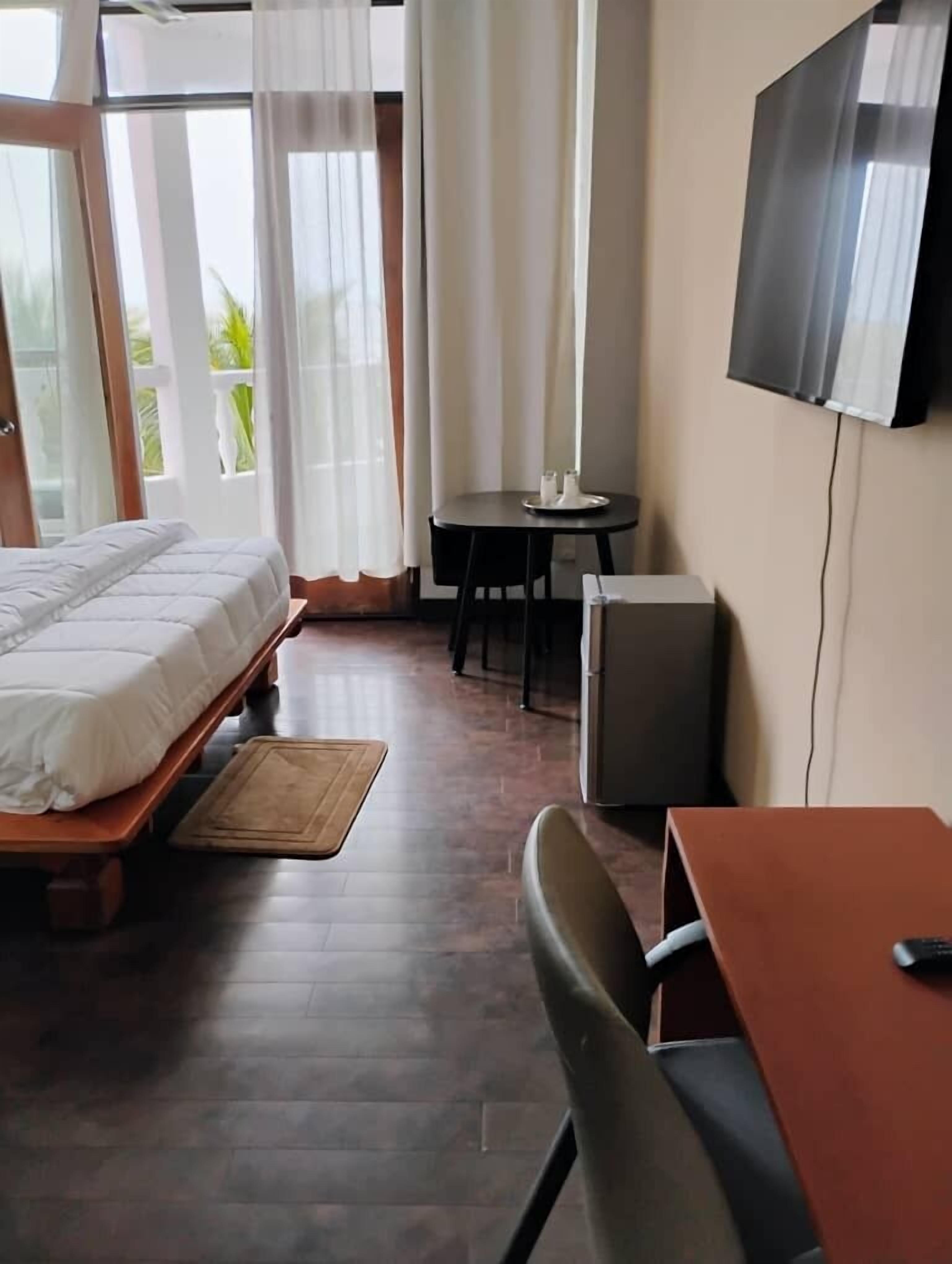 A hotel room with a bed, a desk, a chair, a TV, and a small table with candles.