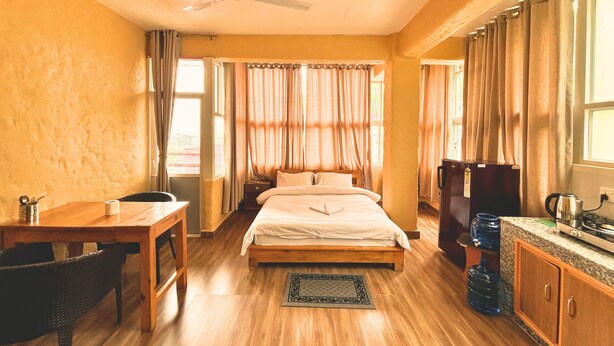 A bedroom with a bed, a desk, a chair, a ceiling fan, and a kitchenette. - Nishan Apartments and Home (Pokhara)