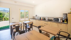 A modern kitchen with wooden cabinets, a countertop with appliances, and a dining area with tables and chairs. - S'Omu e Chicchinu rooms (Cardedu)
