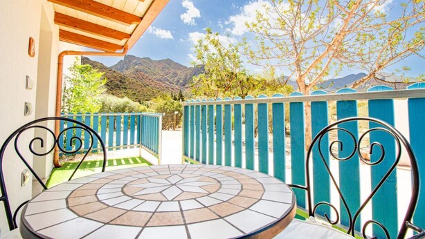 A patio with a tiled table and chairs, a wooden ceiling, and a view of mountains and trees. - S'Omu e Chicchinu rooms (Cardedu)