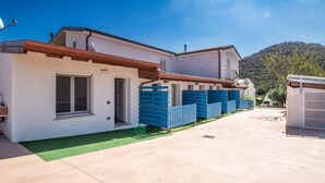 A modern two-story house with a flat roof, a green lawn, and a mountain in the background. - S'Omu e Chicchinu rooms (Cardedu)