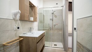 A modern bathroom with a glass shower enclosure, a wooden vanity, and a hairdryer mounted on the wall. - S'Omu e Chicchinu rooms (Cardedu)