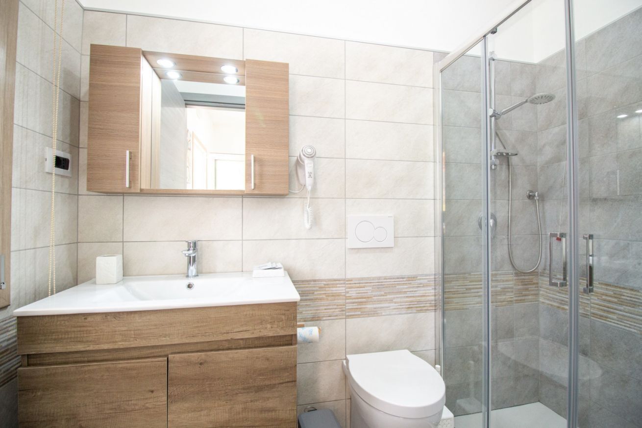 Un baño moderno con tocador de madera, inodoro blanco, cabina de ducha de vidrio y un espejo grande.