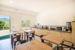 A modern kitchen with wooden cabinets, a countertop with appliances, and a dining area with tables and chairs.