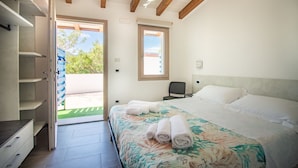A bedroom with a bed, a chair, a desk, and a wardrobe. There is a window and a door leading to an outdoor area. - S'Omu e Chicchinu rooms (Cardedu)