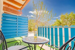 Eine Terrasse mit blauem Zaun, einem runden Tisch, einer Flasche und einem Stuhl.