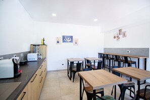 Una cocina moderna con mesas y sillas de madera, una cafetera y un microondas.