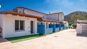A modern two-story house with a flat roof, a green lawn, and a mountain in the background. - S'Omu e Chicchinu rooms (Cardedu)