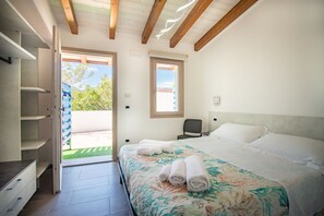 Une chambre à coucher comprenant un lit, une chaise, un bureau et une armoire. Il y a une fenêtre et une porte donnant sur un espace extérieur.