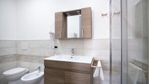 A modern bathroom with a white sink, wooden vanity, and a glass shower enclosure. - S'Omu e Chicchinu rooms (Cardedu)