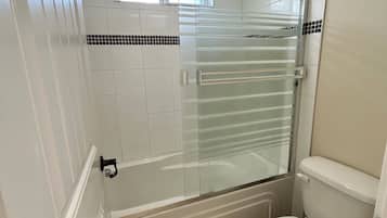 Bathroom features a glass-enclosed shower, bathtub, and white toilet.