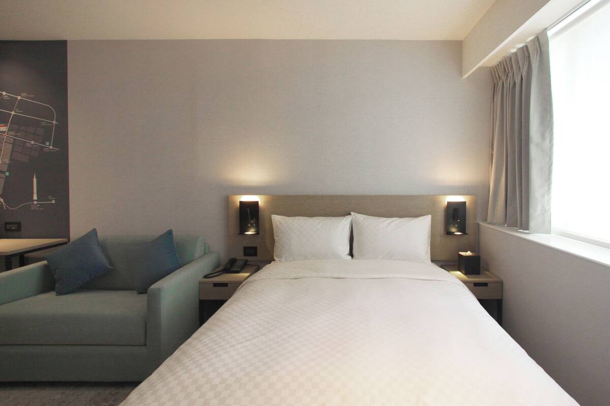 A hotel room with a bed, a nightstand, a lamp, a chair, and a wall-mounted map.