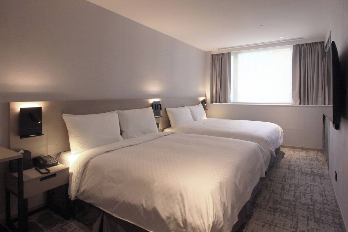 A hotel room with two beds, a desk with a telephone, and a TV mounted on the wall.