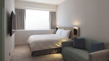 A hotel room with a bed, a green sofa, a TV mounted on the wall, and a window with curtains.