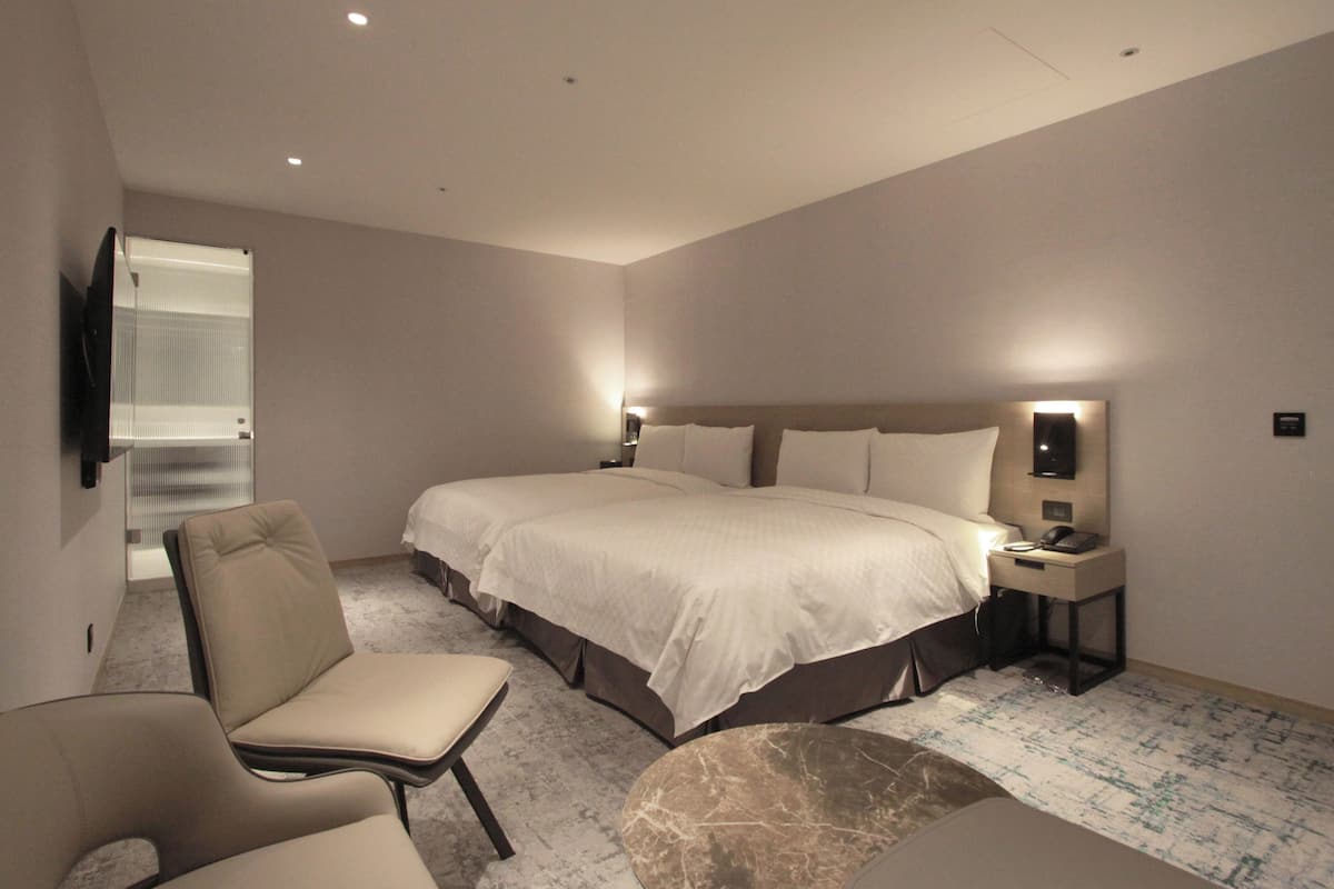 A modern hotel room with a large bed, a bedside table, a chair, and a flat-screen TV.
