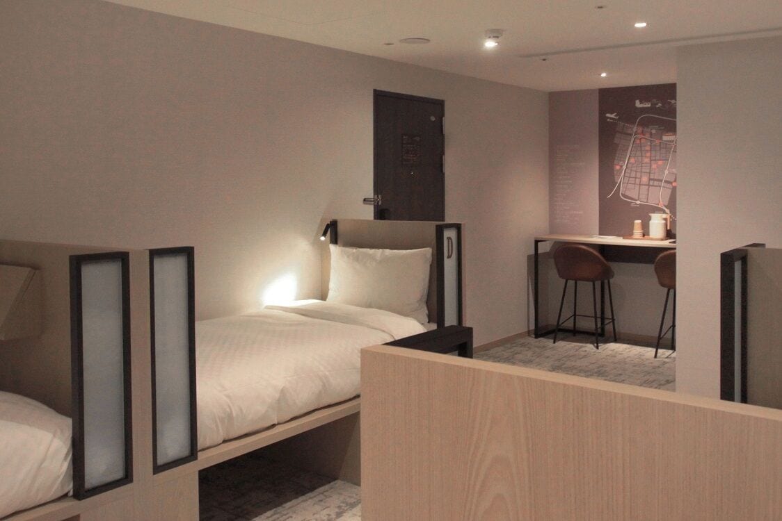 A compact hotel room with a bed, a desk with two chairs, and a map on the wall.