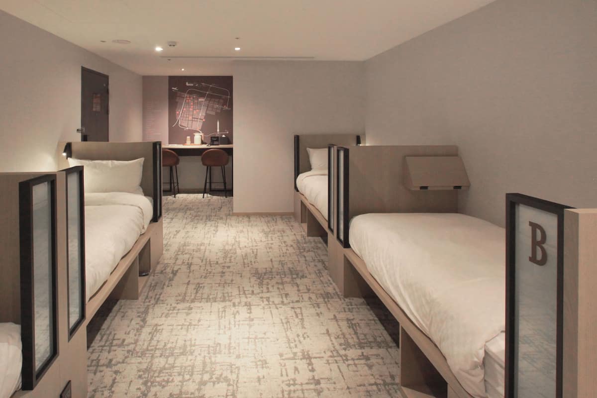A hotel room with two single beds, a desk with a chair, and a small kitchenette.