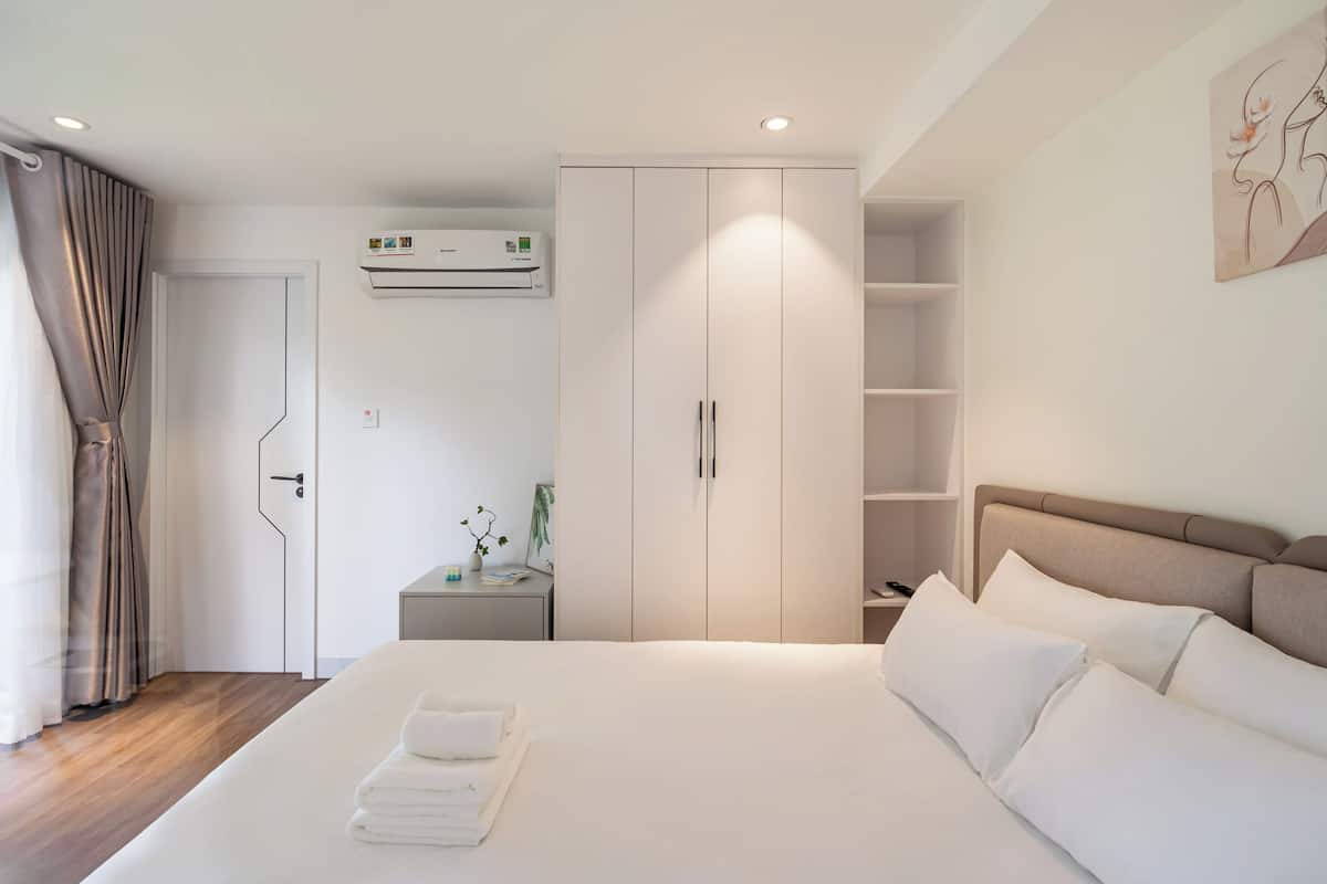 Une chambre d’hôtel moderne avec un lit bien fait, une armoire, une table de chevet avec une lampe et un appareil de climatisation.