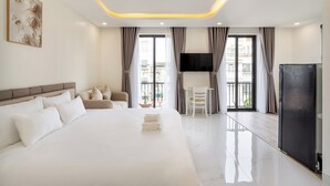 Una habitación de hotel moderna con una cama grande, un área de descanso, un televisor y un balcón con cortinas.