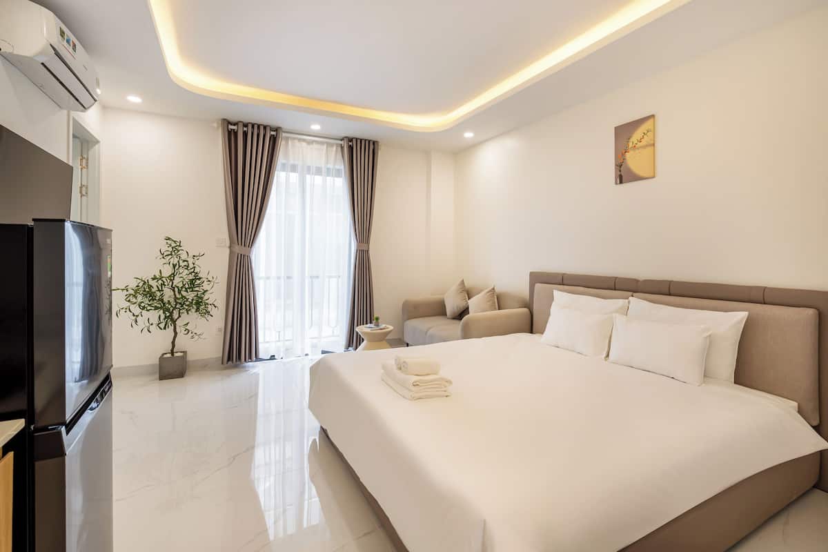 Une chambre d’hôtel moderne avec un grand lit, un téléviseur à écran plat, une plante en pot et une vue sur l’extérieur par la fenêtre.