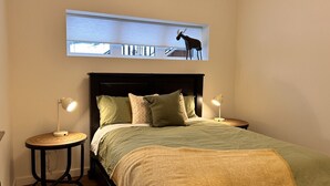A bedroom with a bed, two bedside tables, a window with a view, and a mounted moose sculpture.