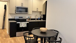 A modern kitchen with a microwave, oven, and sink. There is a dining table with chairs and a wooden bowl on it.