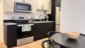 A modern kitchen with a built-in oven, microwave, and refrigerator. There is a dining table with a wooden bowl on it.