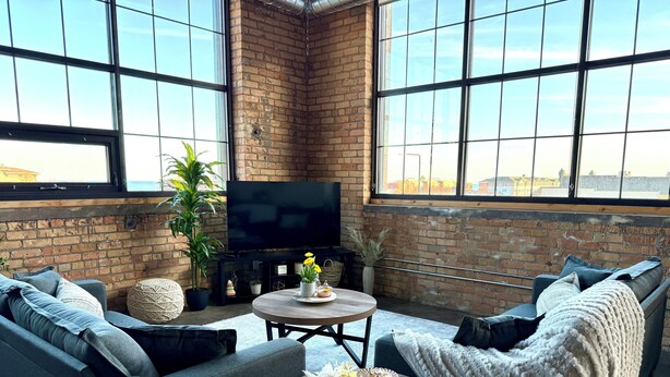 A cozy living room with a brick wall, large windows, and modern furniture. - The Luxe Loft in Canal Park | Boho-Chic (Duluth)