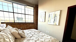 A bedroom with a large bed, a brick wall, and two abstract paintings. - The Luxe Loft in Canal Park | Boho-Chic (Duluth)