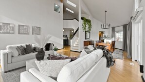 A modern living room with a white sofa, a coffee table, and a dining area with a chandelier.