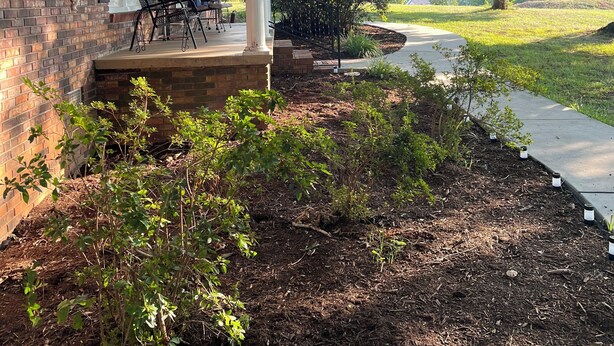 A brick house with a covered porch, outdoor seating, and a garden area with mulch and plants. -  NO CLEANING FEE Century farmhouse on Lake Keowee near Clemson (Seneca)