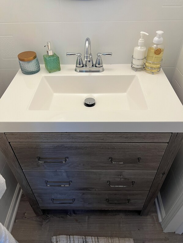 Un baño con un lavabo blanco, dos grifos, un dispensador de jabón y una botella de jabón líquido.