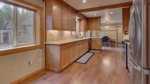 A spacious kitchen with wooden cabinets, a large refrigerator, and a window overlooking a residential area.