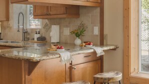 A kitchen with a marble countertop, wooden cabinets, a stainless steel faucet, and two stools.