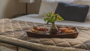 A neatly made bed with a quilted blanket, a tray of pastries, a vase with flowers, and a lamp in a hotel room.