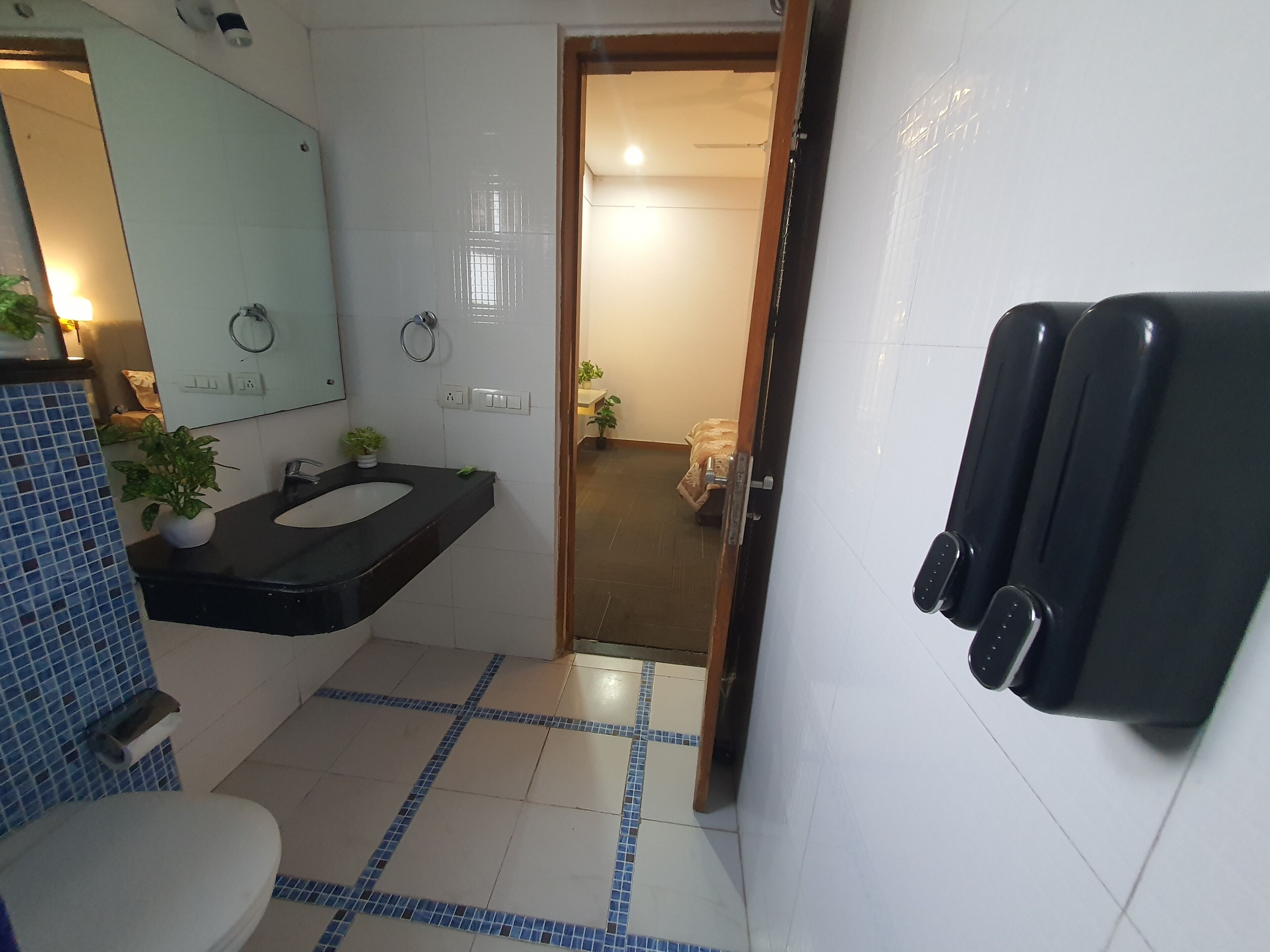 A bathroom with a black sink, white toilet, and a mirror. There are two hand dryers and a potted plant on the counter.