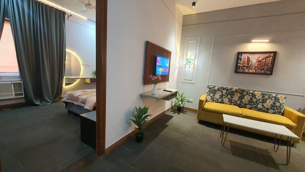 A modern living room with a sofa, a small table, a TV mounted on the wall, and a painting. - Mallenzo suites (Gurugram)