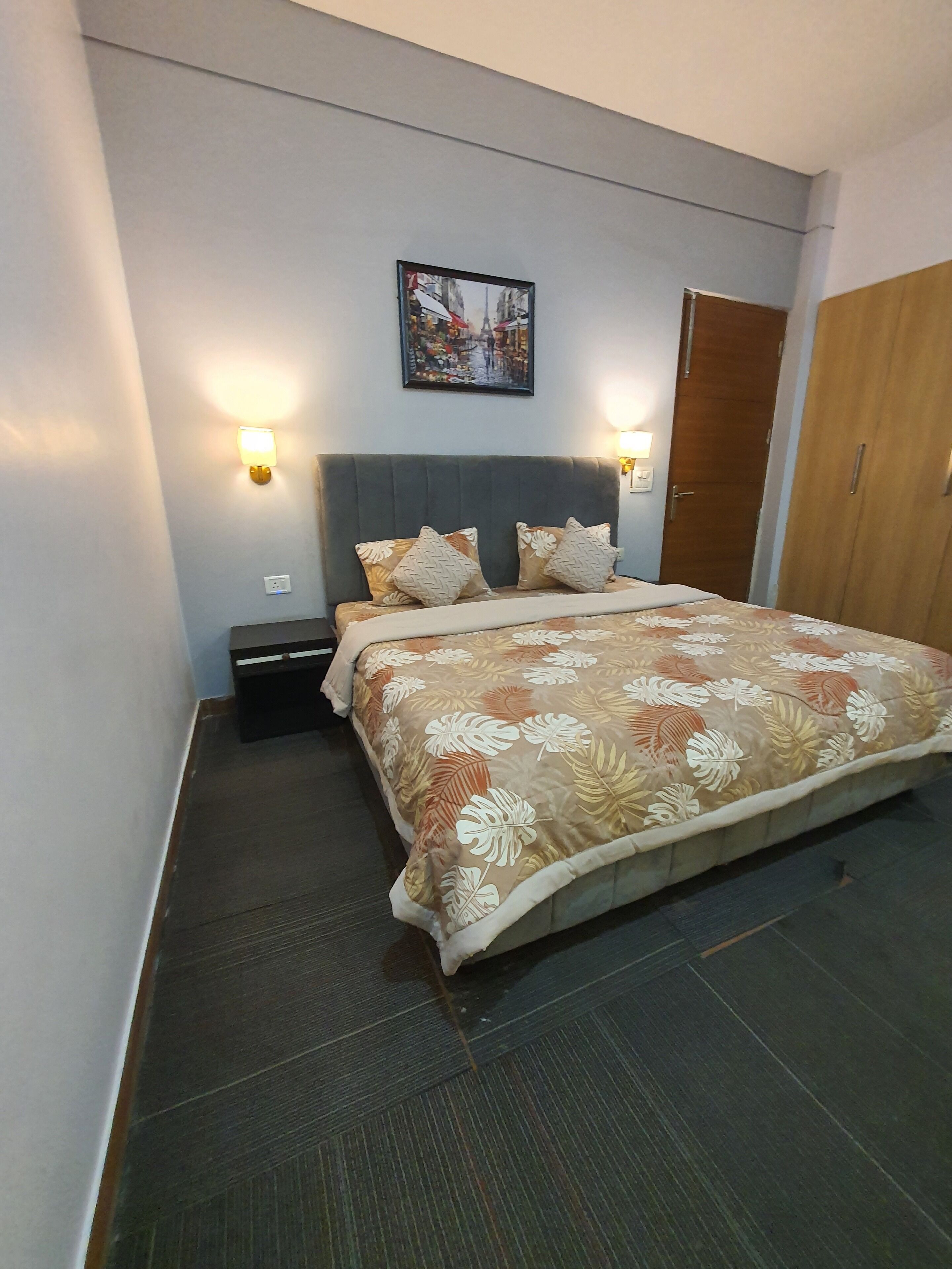 A neatly arranged bedroom with a bed, two bedside tables, a nightstand, a wardrobe, and a wall-mounted picture.