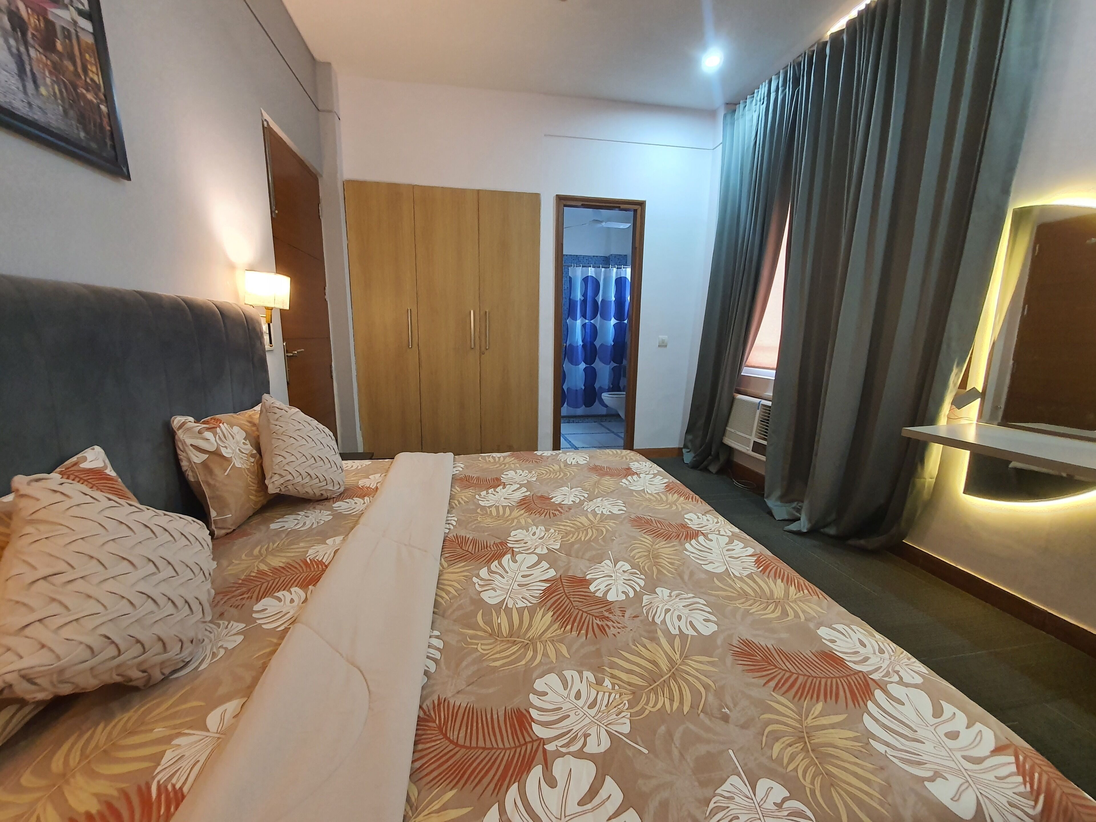 A hotel room with a bed, a wardrobe, a bathroom visible through an open door, and a TV on a stand.