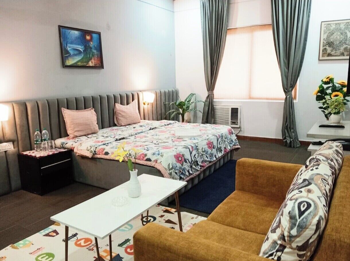 Een hotelkamer met een bed, een bank, een bijzettafeltje, een nachtkastje en een raam met gordijnen.