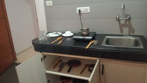 A compact kitchen with a black countertop, a stainless steel sink, and a drawer below containing various utensils. - Mallenzo suites (Gurugram)