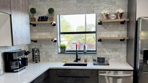 Une cuisine moderne dotée d’un plan de travail en marbre, d’appareils électroménagers en acier inoxydable et d’une fenêtre offrant une vue sur l’extérieur.