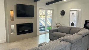 Un salon moderne doté d’un grand canapé d’angle, d’un téléviseur à écran plat fixé au mur, d’un ventilateur de plafond et d’un lave-linge et d’un sèche-linge intégrés.