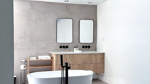 Une salle de bain moderne avec une baignoire sur pieds, un meuble-lavabo en bois et deux miroirs fixés au mur.