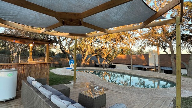 Une terrasse extérieure avec une piscine, une plateforme en bois et un espace salon couvert agrémenté de coussins.