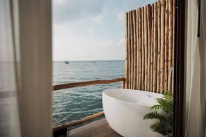 A bathroom with a large white bathtub, a wooden fence, and a view of the sea. - De' Ocean land (Koh Lan)