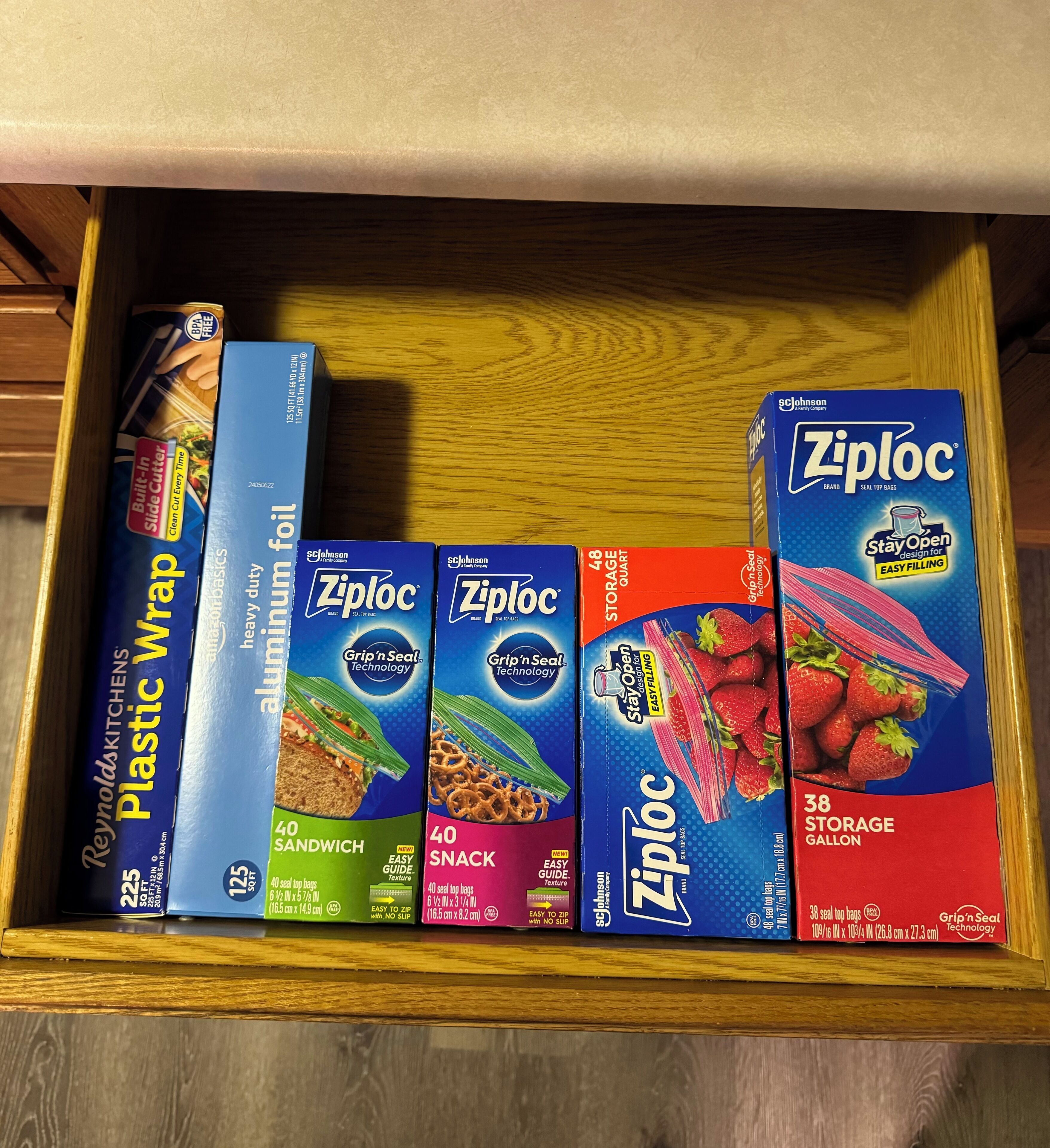 A drawer containing various plastic wrap products including Reynolds Kitchens Plastic Wrap, Ziploc brand seal top bags, and Ziploc brand seal top bags with a 38-gallon capacity.