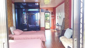 A room with two beds, a small table, a sofa, and a sliding glass door leading to an outdoor area. - Pirate Galeon (Carcar)