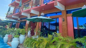 A multi-story building with balconies, large windows, and outdoor seating with umbrellas. - Pirate Galeon (Carcar)