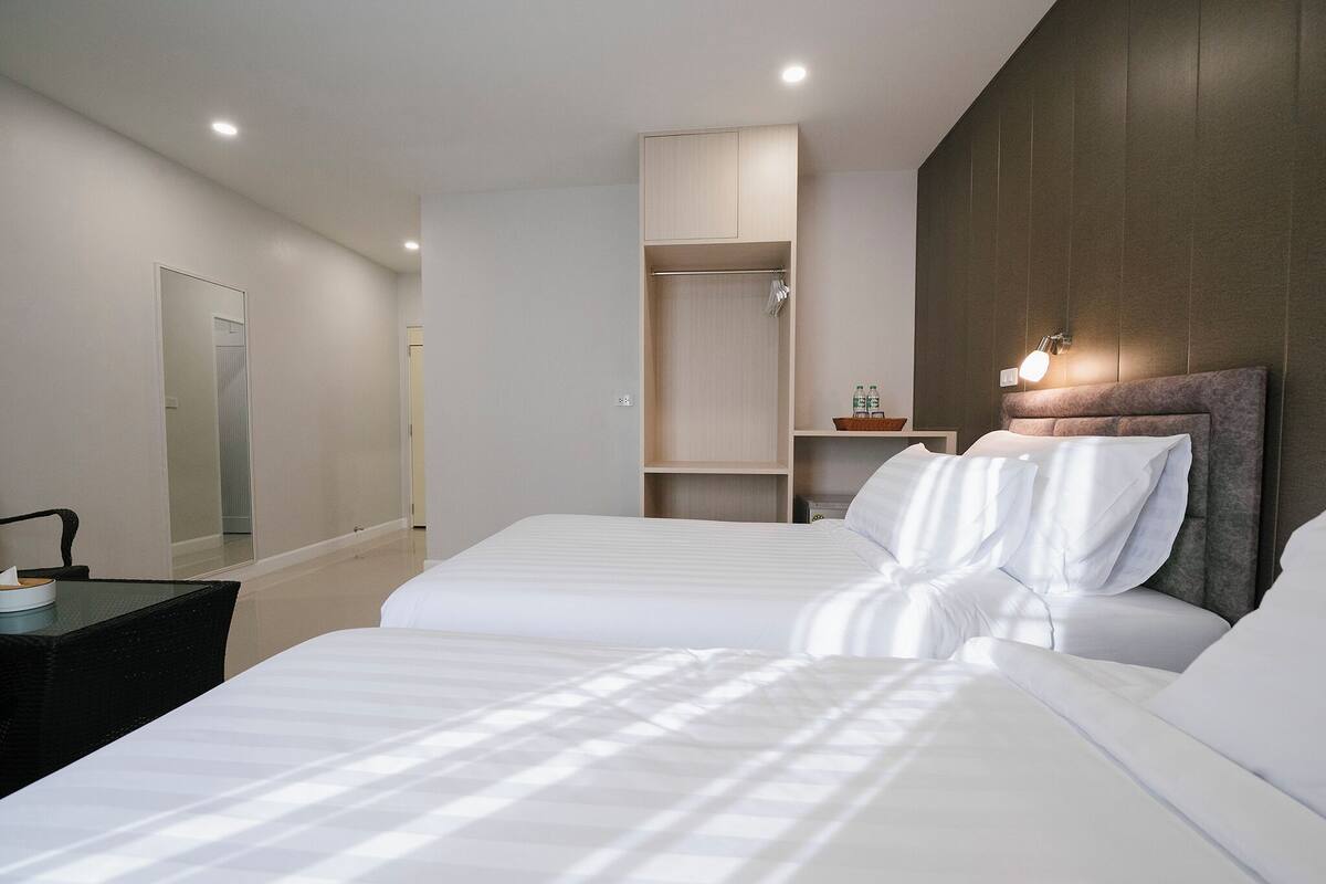 A hotel room with two beds, a bedside table, a mirror, a wardrobe, and a nightstand with a lamp.